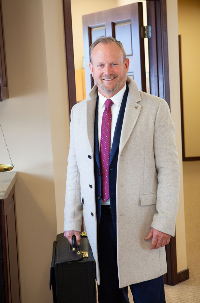 Greg Wohletz standing with jacket holding a briefcase